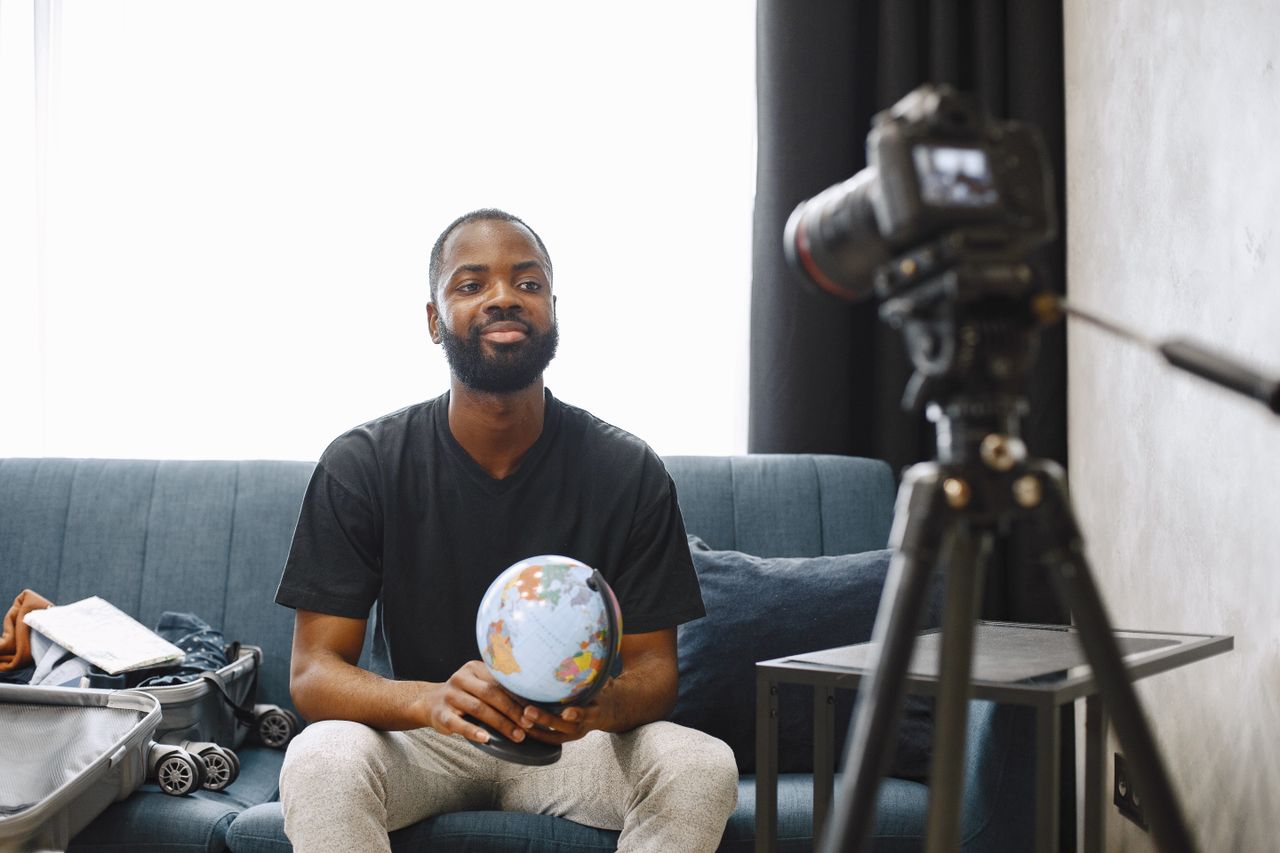 A man holding a globe sits in front of a camera, creating video content from his home studio.