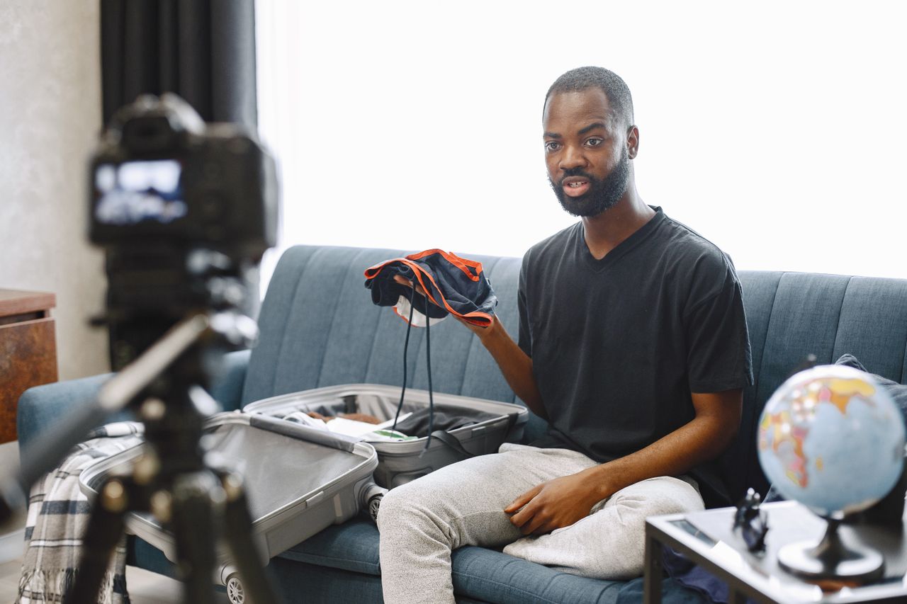 Offerings A vlogger records a travel vlog while unpacking a suitcase indoors with camera setup.