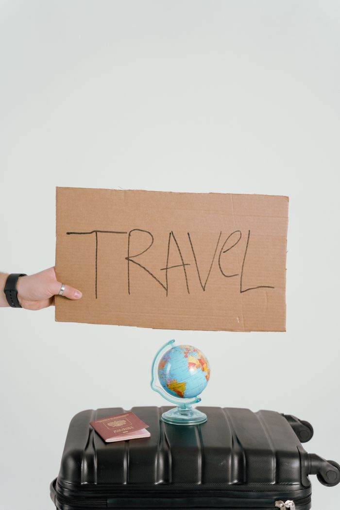 Creative travel concept featuring a cardboard sign, globe, passport, and suitcase against a white background.